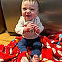 Blake joined the competition — help win amazing prizes! baby, barefoot, blanket, child, clothing, face, feet, floor, hands, happy, indoor, kitchen, long_sleeve_shirt, pants, person, portrait, red_blanket, sitting, smile, wood_floor