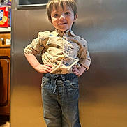Colson is registered to the contest to win money with this photo: child, boy, standing, shirt, dinosaurs, jeans, kitchen, refrigerator, smiling, hands_on_hips, casual_clothing, indoor, wooden_floor, appliance, portrait, happy, young, home, person, cute
