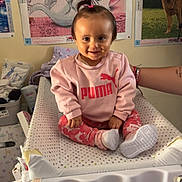 Maëlyne participe au concours pour gagner de l'argent avec cette photo : toddler, child, baby, pink_clothing, puma_logo, socks, changing_table, indoor, poster, toy, room, smiling, hair_tie, person, baby_supplies, diapers, sitting, face, cute, happy