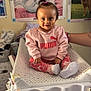toddler, child, baby, pink_clothing, puma_logo, socks, changing_table, indoor, poster, toy, room, smiling, hair_tie, person, baby_supplies, diapers, sitting, face, cute, happy