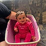 baby, child, pink_clothing, laundry_basket, smiling, indoor, couch, patterned_fabric, person, hand, seated, happy, short_hair, window, supporting_arm, home, casual, cute, infant, human