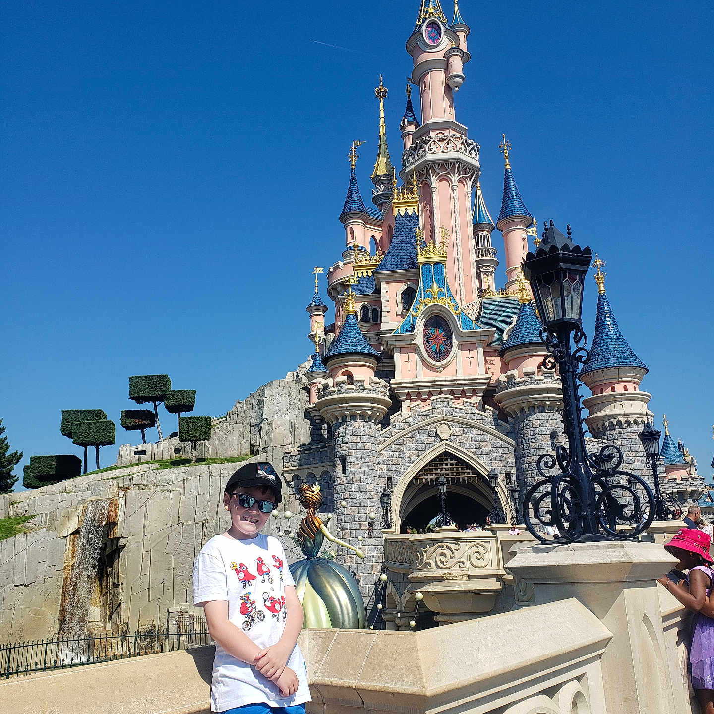 Baptiste participe au concours pour gagner de l'argent avec cette photo : accessories, amusementpark, architecture, boy, building, castle, child, clocktower, clothing, fortress, fun, glasses, hat, male, person, shorts, spire, t_shirt, themepark, tower