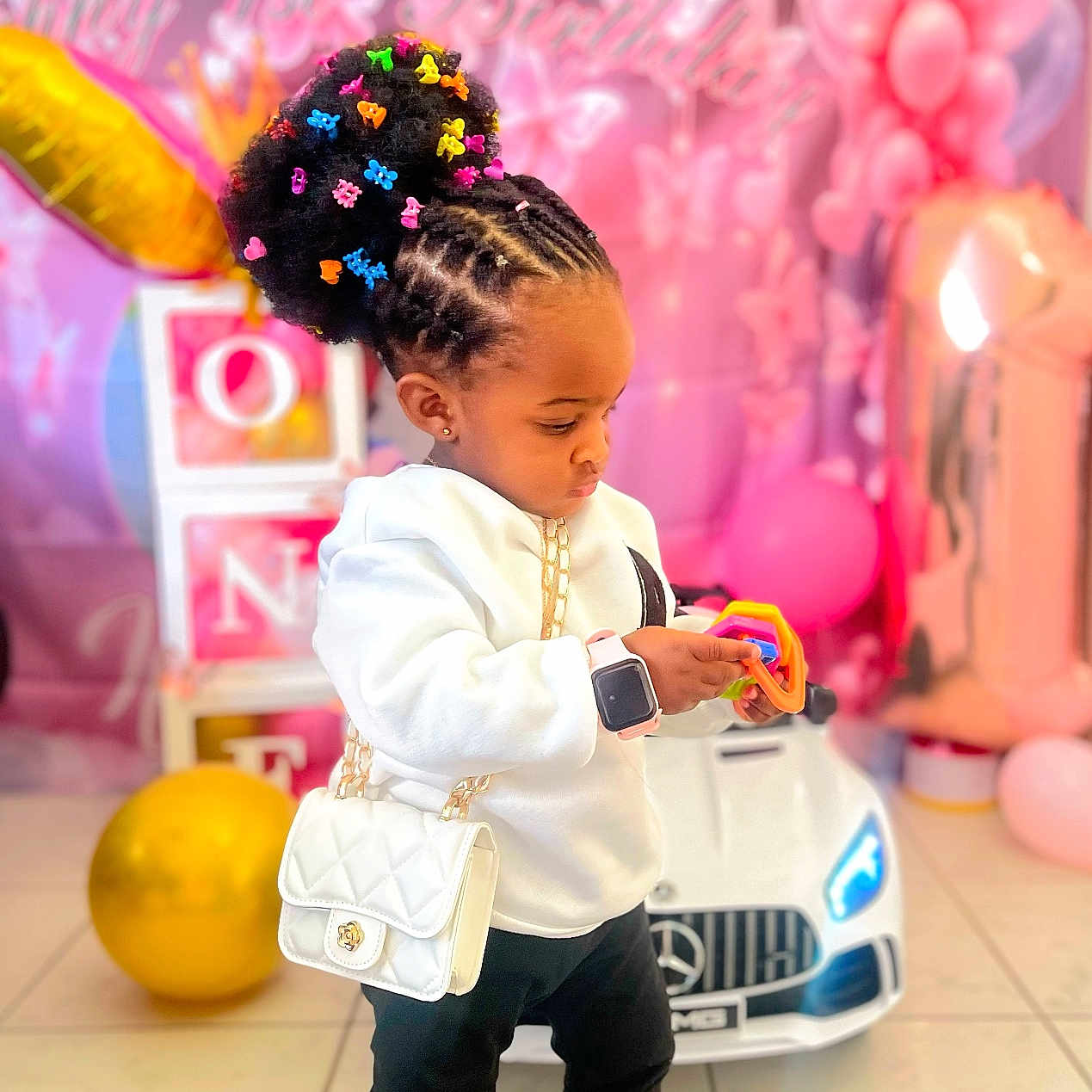 Ifunanya a rejoint le concours — aidez-le/la à gagner de superbes lots ! balloons, birthday, blocks, boots, car_toy, celebration, child, colorful, cornrows, cute, floor_tiles, focused, hair_clips, indoor, party_decorations, pink, smartwatch, toddler, toy, white_purse
