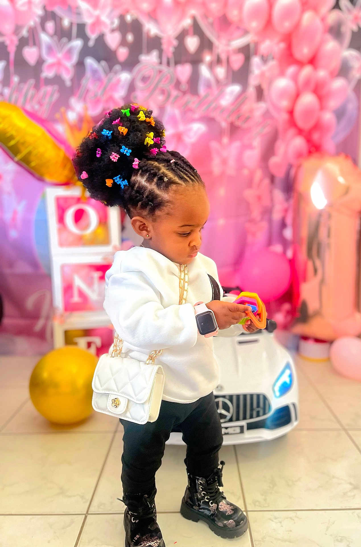 Ifunanya a rejoint le concours — aidez-le/la à gagner de superbes lots ! toddler, child, toy, birthday, balloons, pink, white_purse, smartwatch, boots, hair_clips, cornrows, indoor, car_toy, floor_tiles, party_decorations, blocks, colorful, cute, focused, celebration