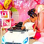 african_american_child, balloons, birthday_party, butterflies, celebration, child_playing, colorful_hair_clips, cute, decorations, event, floor, happy, indoor, party, pink_backdrop, small_car, toddler, toy_car, watch, white_dress