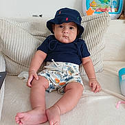 Kelvin a rejoint le concours — aidez-le/la à gagner de superbes lots ! baby, child, infant, hat, shorts, shirt, couch, pillow, toy, indoor, person, feet, hand, face, skin, clothing, seated, looking, cute, home