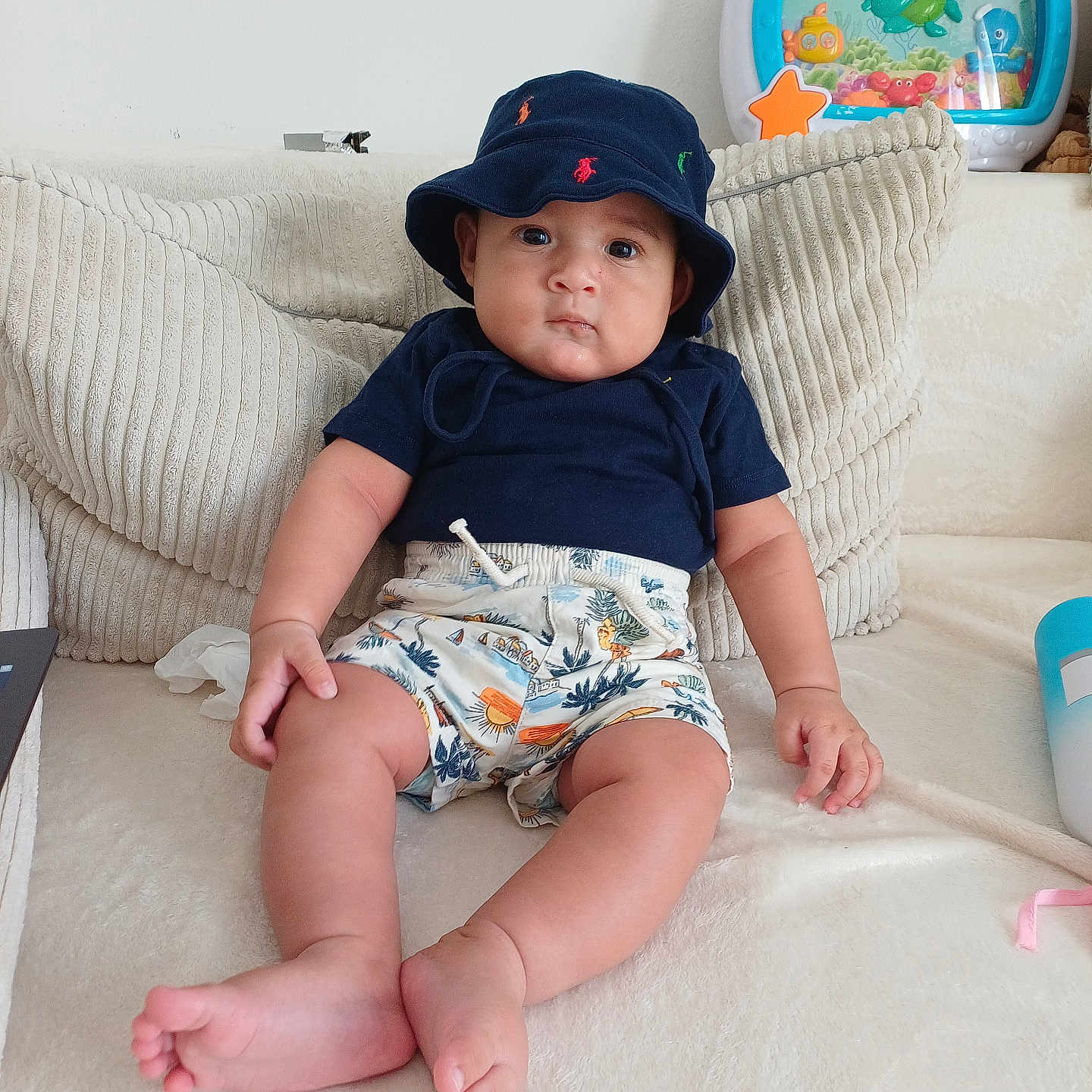 Kelvin a rejoint le concours — aidez-le/la à gagner de superbes lots ! baby, child, clothing, couch, cute, face, feet, hand, hat, home, indoor, infant, looking, person, pillow, seated, shirt, shorts, skin, toy