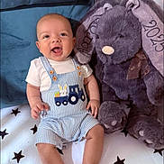 Aaron is registered to the contest to win money with this photo: baby, child, smiling, overalls, striped_clothing, white_tshirt, plush_toy, teddy_bear, blanket, stars, sitting, cute, happy, indoor, soft_toy, ribbon, embroidery, infant, person, face