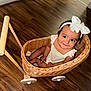 baby, child, wicker_basket, bow, headband, smile, wooden_floor, toy_cart, happy, indoors, cute, sitting, person, infant, playful, white_clothing, flooring, basket, wheel, portrait