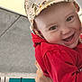 apparel, baby, child, cute, expression, eyes, face, hand, happy, hat, headwear, holding, hoodie, indoor, joyful, person, portrait, red_clothing, smiling, young_child