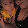 baby, infant, adult, parent, selfie, portrait, cuddling, holding, face, smiling, sleepy, yellow_shirt, black_clothing, indoors, close_up, family, baby_clothing, arms, dim_lighting, nike