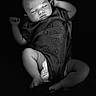 baby, newborn, sleeping, portrait, black_and_white, infant, onesie, diaper, peaceful, indoors, close_up, face, arms_raised, lying_down, soft_lighting, dark_background, baby_clothing, relaxed, photography, monochrome