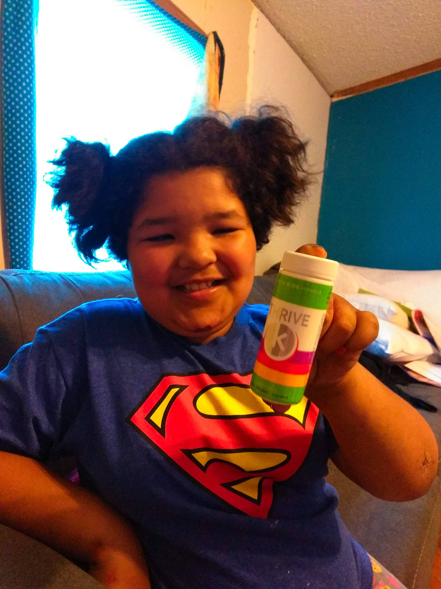 Isis is registered to the contest to win money with this photo: arm, azure, child, electric_blue, finger, fun, gesture, hairstyle, hand, happy, joy, leisure, mouth, person, plastic, plastic_bottle, room, shoulder, smile, superman