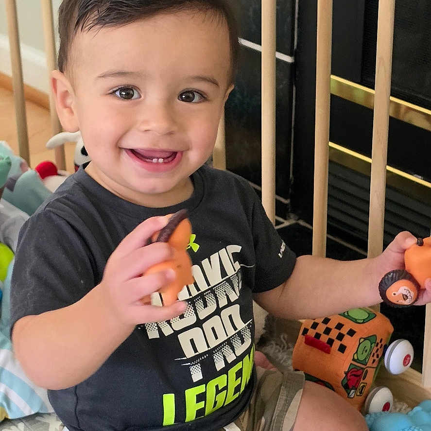 Bentley joined the competition — help win amazing prizes! toddler, child, smiling, portrait, sitting, playpen, toys, giraffe_toy, toy_car, indoor, home, baby, happy, short_hair, t_shirt, shorts, play_mat, kneeling, colorful, photograph