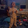 child, toddler, smiling, happy, standing, pajamas, indoors, bedroom, toys, stuffed_animals, carpet, couch, pillows, television, portrait, full_body, thumbs_up, playroom, dim_lighting, home