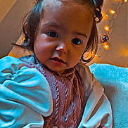 Ménsiya participe au concours pour gagner de l'argent avec cette photo : toddler, child, pigtails, sweater, puffed_sleeves, indoors, fairy_lights, ornaments, blanket, curly_hair, cute, warm_lighting, portrait, baby, soft_texture, decorations, smiling, face, hands, cozy