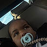 child, pacifier, car_seat, leather, window, sky, face, infant, baby, closeup, seat, clothing, resting, thoughtful, indoors, transportation, leisure, young_child, person, portrait
