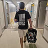Emery joined the competition — help win amazing prizes! man, baby, car_seat, hospital, hallway, tshirt, shorts, walking, floor, door, sign, light, person, infant, indoor, baby_clothes, hospital_room, parent, child, back_view
