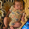 baby, infant, sleeping, blanket, floral_clothing, onesie, portrait, face, cozy, indoor, tablet, screen, technology, lying_down, sitting, barefoot, hands, legs, warm_lighting, home