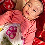 baby, infant, face_paint, blanket, red, pink, cardigan, dress, flower_embroidery, plush, soft, cute, child, lying_down, indoors, portrait, skin, hand, head, smile