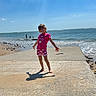 Rose participe au concours pour gagner de l'argent avec cette photo : barefoot, beach, casual_clothing, child, clouds, concrete, girl, ocean, outdoor, pier, sand, sea, shorts, sky, smiling, summer, sunlight, tshirt, vacation, water