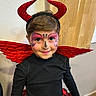 child, face_paint, costume, devil_horns, red_wings, smiling, black_shirt, red_skirt, indoor, portrait, cute, happy, headband, makeup, person, holiday, festive, party, young, celebration