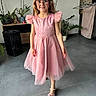 Rose participe au concours pour gagner de l'argent avec cette photo : child, clothing, decor, floor_tile, footwear, furniture, girl, glasses, hair, home, indoor, living_room, person, pink_dress, plant, smile, speaker, standing, television, towel