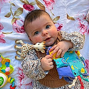 Clara participe au concours pour gagner de l'argent avec cette photo : baby, child, toy, giraffe_toy, fabric_book, floral_blanket, cute, infant, portrait, hand, smile, clothing, patterned_dress, play, lying_down, indoor, colorful, soft_toys, young_child, happy