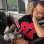 woman, sleeping, dog, french_bulldog, pet, chair, jersey, glasses, porch, window, outdoor, relaxing, nap, black_clothing, red_numbers, furniture, hand, resting, calm, domestic
