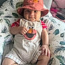 baby, child, smiling, hat, overalls, elmo, red, cushion, leaf_pattern, indoor, cute, skin, hand, legs, face, clothing, seated, comfort, playful, infant