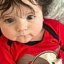 baby, child, closeup, curly_hair, cute, expression, eyes, face, indoors, infant, mouth, nose, patterned_background, person, pillow, portrait, red_clothing, skin, toddler, young