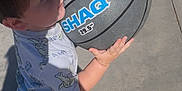 Josiah is registered to the contest to win money with this photo: activity, basketball, casual_clothing, child, concrete, daylight, holding, outdoor, person, play, recreation, shadow, shirt, shorts, sports, summer, sunlight, toy, white_shoes, young_child