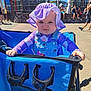 baby, child, purple_hat, blue_stroller, outdoor, sunny, people, concrete, fence, casual_clothing, daylight, hat, person, purple_shirt, denim_overalls, expression, grip, summer, background, recreation_area