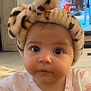 Juna a rejoint le concours — aidez-le/la à gagner de superbes lots ! baby, infant, headband, bow, leopard_print, flamingo_pattern, clothing, face, eyes, cute, indoor, television, furniture, home, child, portrait, expression, soft_texture, curious, young
