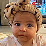 baby, infant, headband, bow, leopard_print, flamingo_pattern, clothing, face, eyes, cute, indoor, television, furniture, home, child, portrait, expression, soft_texture, curious, young