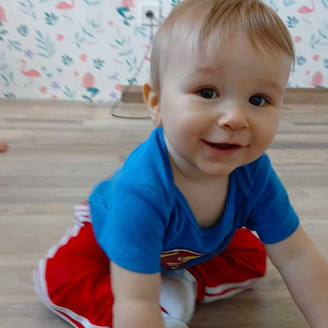 Tyler a rejoint le concours — aidez-le/la à gagner de superbes lots ! baby, blue_shirt, child, crawling, curious, face, flamingo, floor, footwear, hair, hand, happy, indoor, pattern, red_pants, skin, smiling, toddler, wallpaper, wooden_floor