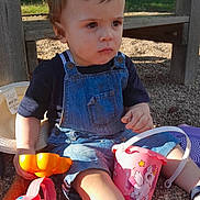 Zayn participe au concours pour gagner de l'argent avec cette photo : toddler, child, denim_overalls, toy, pink_bucket, unicorn, gravel, playground, outdoor, sunlight, shade, serious_expression, blue_shoes, hat, wooden_structure, person, kid, summer, casual_clothing, playtime