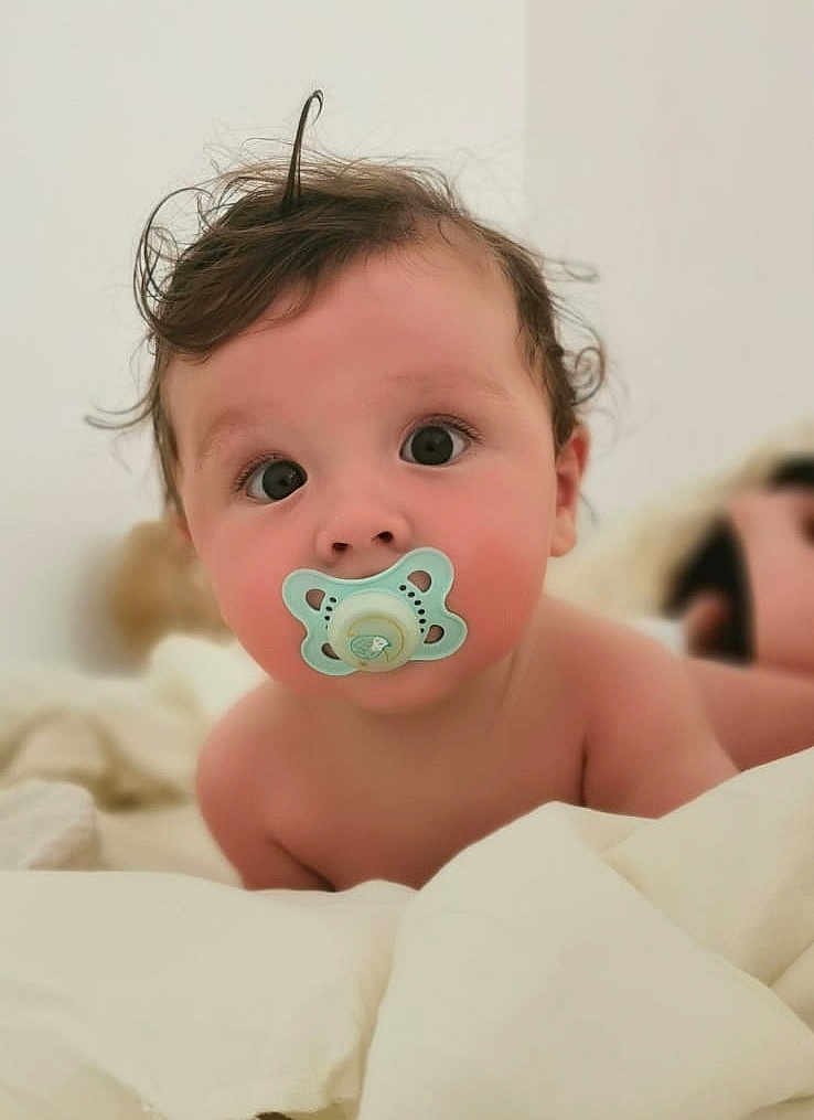 Nelyo a rejoint le concours — aidez-le/la à gagner de superbes lots ! baby, pacifier, curly_hair, blanket, indoors, close_up, infant, face, skin, cute, child, lying_down, soft_light, expression, young, portrait, bed, comfort, eyes, toddler