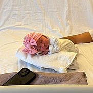 Amelya a rejoint le concours — aidez-le/la à gagner de superbes lots ! newborn, baby, sleeping, pink_bow, blanket, white_clothing, infant, bed, arm, smartphone, soft_texture, resting, peaceful, indoors, cozy, portrait, child, human, tender_moment, closeup