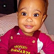 Azlyn is registered to the contest to win money with this photo: baby, child, smile, face, clothing, overalls, text, maroon, blanket, indoor, portrait, cute, eyes, button, sitting, person, infant, young_child, happy, closeup