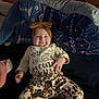 baby, smiling, headband, bow, clothing, patterned_pants, blanket, blue, cute, infant, lying_down, happy, indoor, child, person, face, cozy, soft_lighting, casual, text_on_clothing