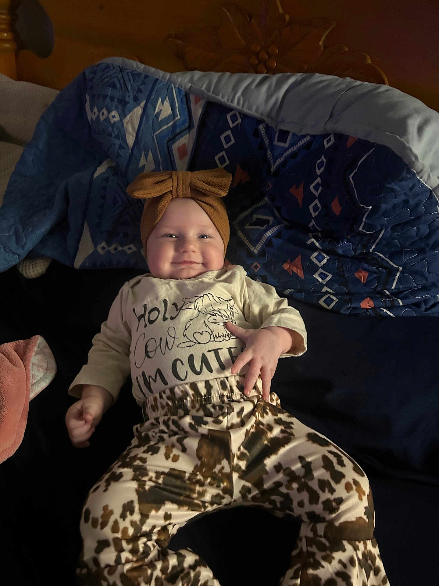Azlynn is registered to the contest to win money with this photo: baby, smiling, headband, bow, clothing, patterned_pants, blanket, blue, cute, infant, lying_down, happy, indoor, child, person, face, cozy, soft_lighting, casual, text_on_clothing