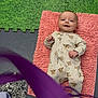 Reggie is registered to the contest to win money with this photo: baby, infant, smiling, onesie, pink_mat, green_floor, foam_tiles, playful, cute, lying_down, child, floor, texture, animal_print, purple_object, footwear, blanket, indoor, happy, portrait