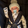 baby, infant, car_seat, pacifier, hat, knit_hat, pom_pom, onesie, bear_pattern, child, cute, wide_eyes, straps, safety_harness, indoor, soft_lighting, portrait, person, warm_clothing, seated