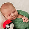 baby, newborn, sleeping, green_blanket, crochet_toy, pokeball, infant, cute, soft_texture, wrapped, handmade, peaceful, child, portrait, indoors, knitted, smiling, resting, cozy, closeup