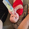 Eryk is registered to the contest to win money with this photo: baby, bottle, milk, red_clothing, couch, cushion, infant, feeding, hand, arm, person, indoor, relaxing, cute, child, portrait, skin, face, eyes, home