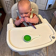 Eryk is registered to the contest to win money with this photo: baby, high_chair, spoon, measuring_spoon, kitchen, laundry_basket, floor, door, appliance, curious, child, seat_belt, wooden_legs, plastic_tray, infant, indoor, cooking_utensil, tableware, eating, young_child