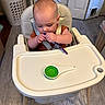 baby, high_chair, spoon, measuring_spoon, kitchen, laundry_basket, floor, door, appliance, curious, child, seat_belt, wooden_legs, plastic_tray, infant, indoor, cooking_utensil, tableware, eating, young_child