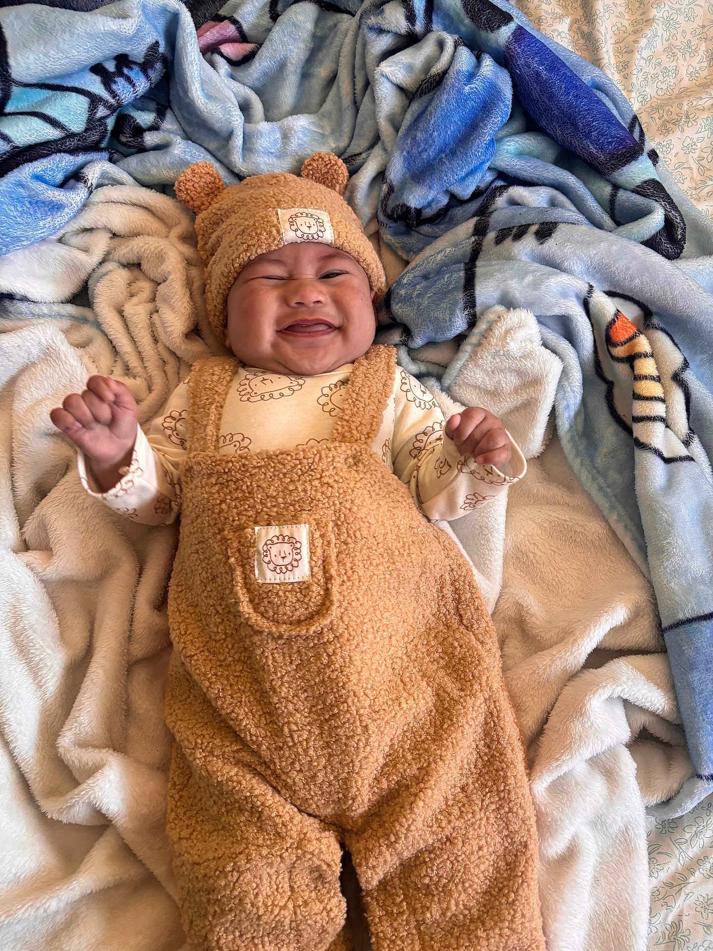 Ezekiel is registered to the contest to win money with this photo: baby, infant, smiling, blanket, beanie, hat, teddy_outfit, plush_overall, onesie, cozy, lying_down, bed, bedding, soft_texture, cute, portrait, hands_up, happy, nursery, grin