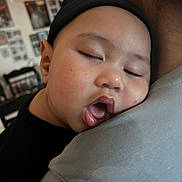 Ezekiel joined the competition — help win amazing prizes! baby, infant, sleeping, drooling, face, beanie, hat, shoulder, parent, close_up, portrait, tongue, cheek, indoor, home, cozy, blurred_background, black_clothing, napping, photowall